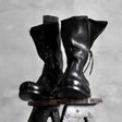 Pair of black high shaft deconstructed leather boots displayed on stool showing zipper and sculptural silhouette, Alternative Darkwear