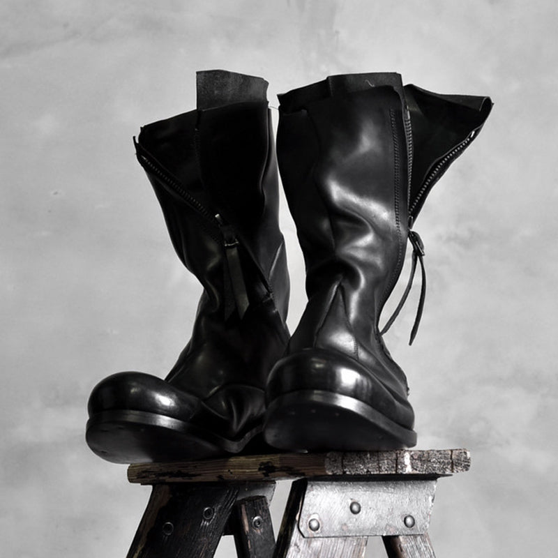 Pair of black high shaft deconstructed leather boots displayed on stool showing zipper and sculptural silhouette, Alternative Darkwear