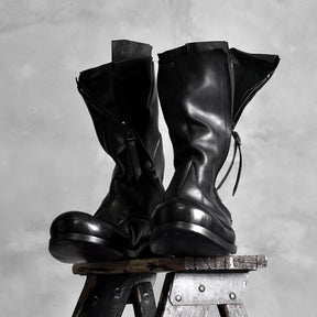 Pair of black high shaft deconstructed leather boots displayed on stool showing zipper and sculptural silhouette, Alternative Darkwear